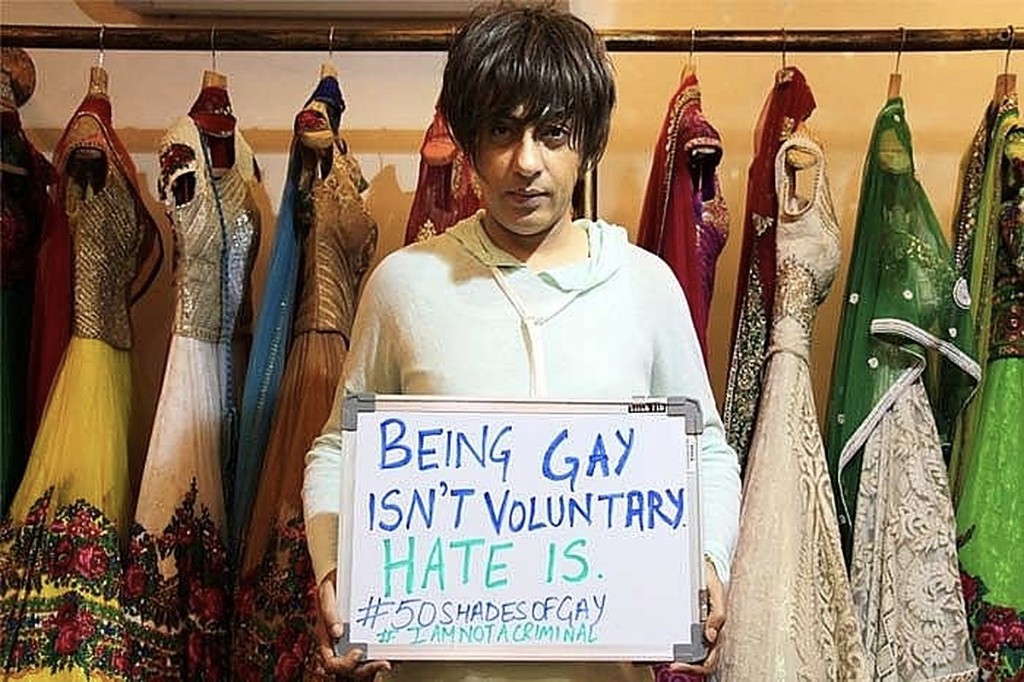 Fashion designer Rohit Verma holding a whiteboard that reads Being gay isn't voluntary, hate is